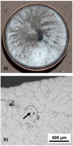 Figure 1. a) Photograph of the as-solidified top surface of a sample of AM-HP2 cast in air and b) an optical photomicrograph near the ‘free’ surface of a section through the diameter of the casting shown in (a) and showing a very limited extent of oxidation.